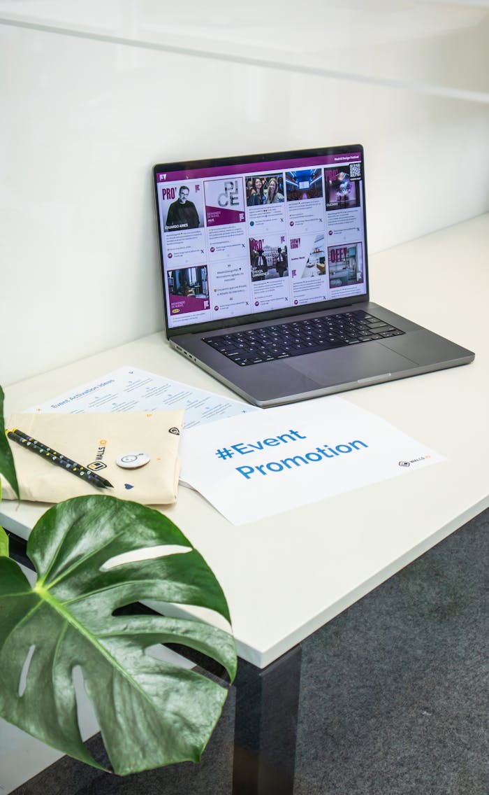 Clean office space with a laptop displaying social media, papers, and a plant for event promotion.